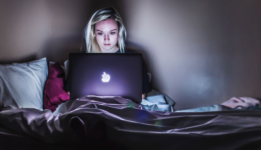 Young girl sitting on her bed in the dark with a bright laptop