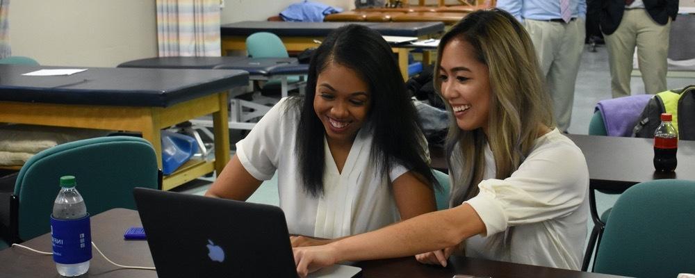 Girls laughing and looking at a macbook